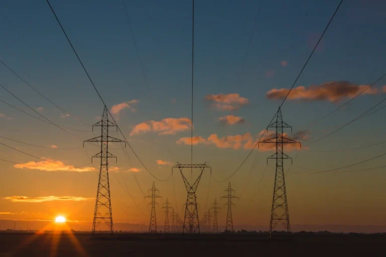 Power grid transmission lines at sunset with AI grid management visualization — smart grid AI balances electricity supply an