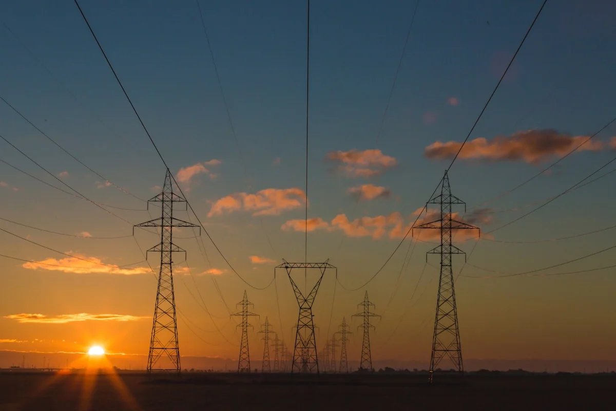 Power grid transmission lines at sunset with AI grid management visualization — smart grid AI balances electricity supply an